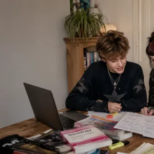 Two A-level Sociology students studying together at home with Sociology textbooks, handwritten notes, highlighters and a laptop